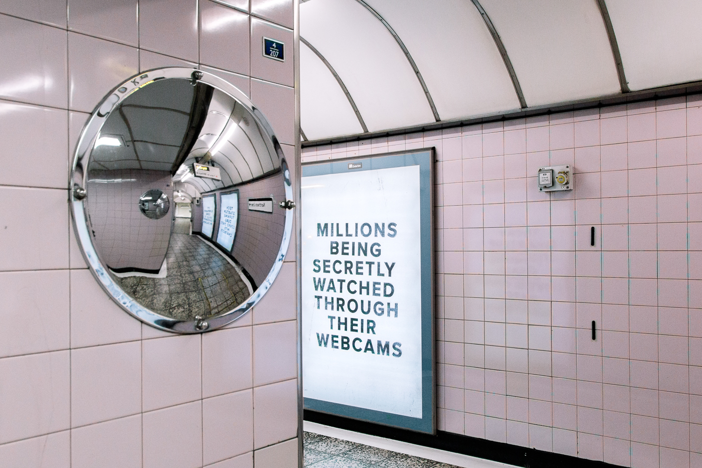 Pop-up Netflix - Black Mirror à Old Street Station, Londres. Un miroir rond dans un couloir devant un panneau "Millions being secretly watched through their webcam" 
